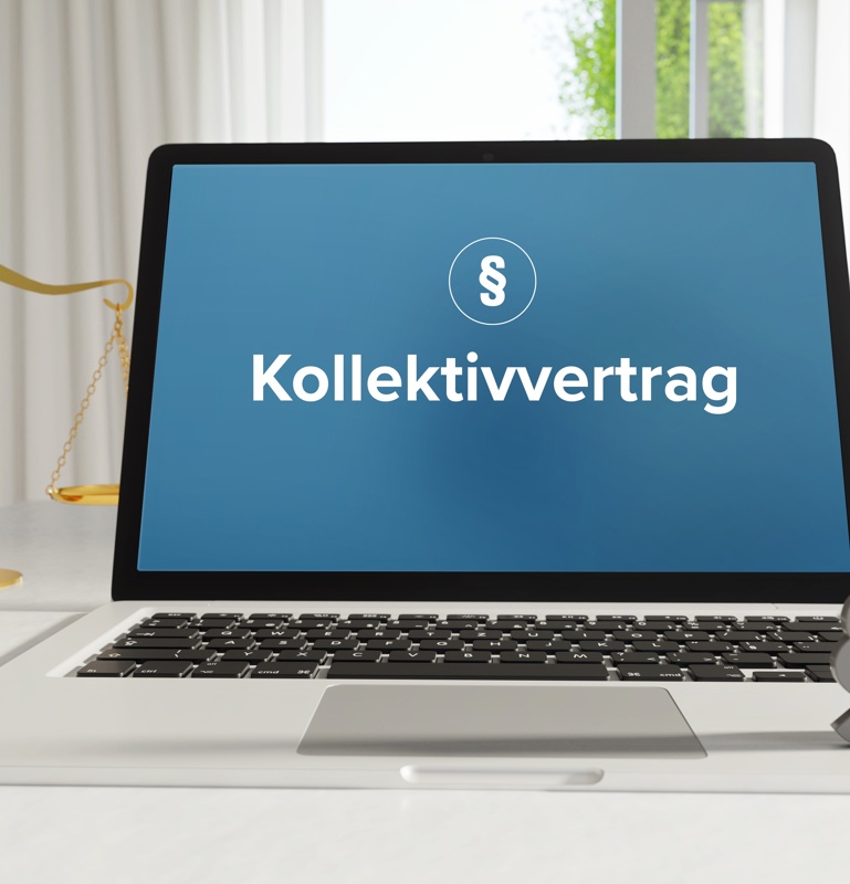 Laptop im Büro mit Begriff Kollektivvertrag auf dem Monitor - daneben Paragraf und Waage